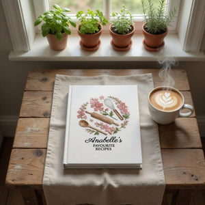 Personalized hand embroidered recipe book featuring pink floral wreath with rolling pin, whisk and wooden spoon on a white linen cover.
