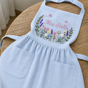 Personalized hand embroidered linen apron featuring colorful wildflowers, butterflies, lavender blooms, and custom name embroidery.