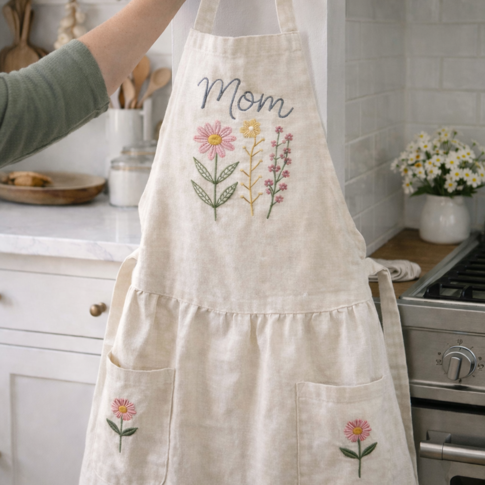 Personalized hand embroidered linen apron featuring pink wildflowers, botanical floral bouquet embroidery, custom name personalization, and floral pocket details.