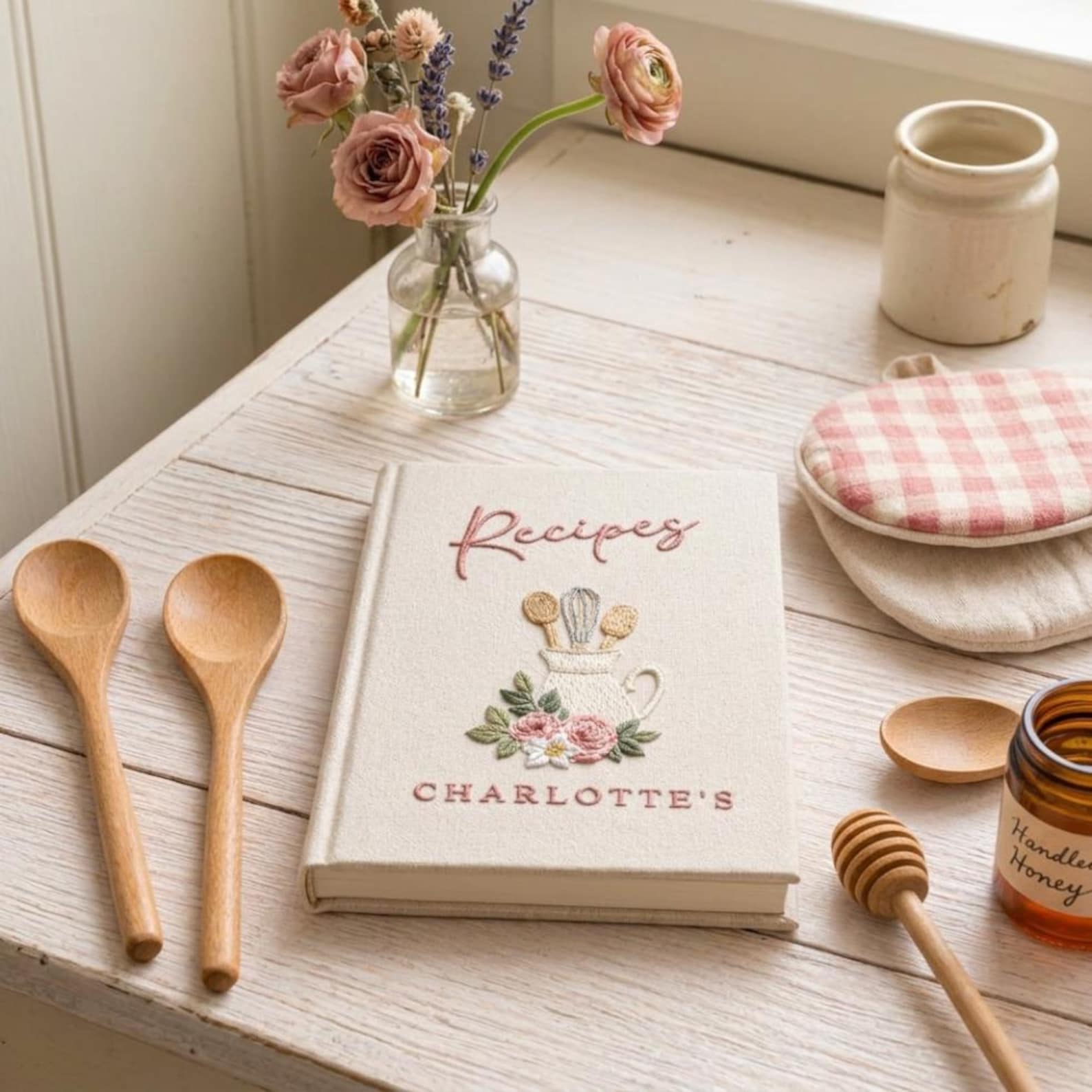 Hand embroidered recipe book featuring a vintage utensil pitcher with pink roses and personalized name on a linen cover.