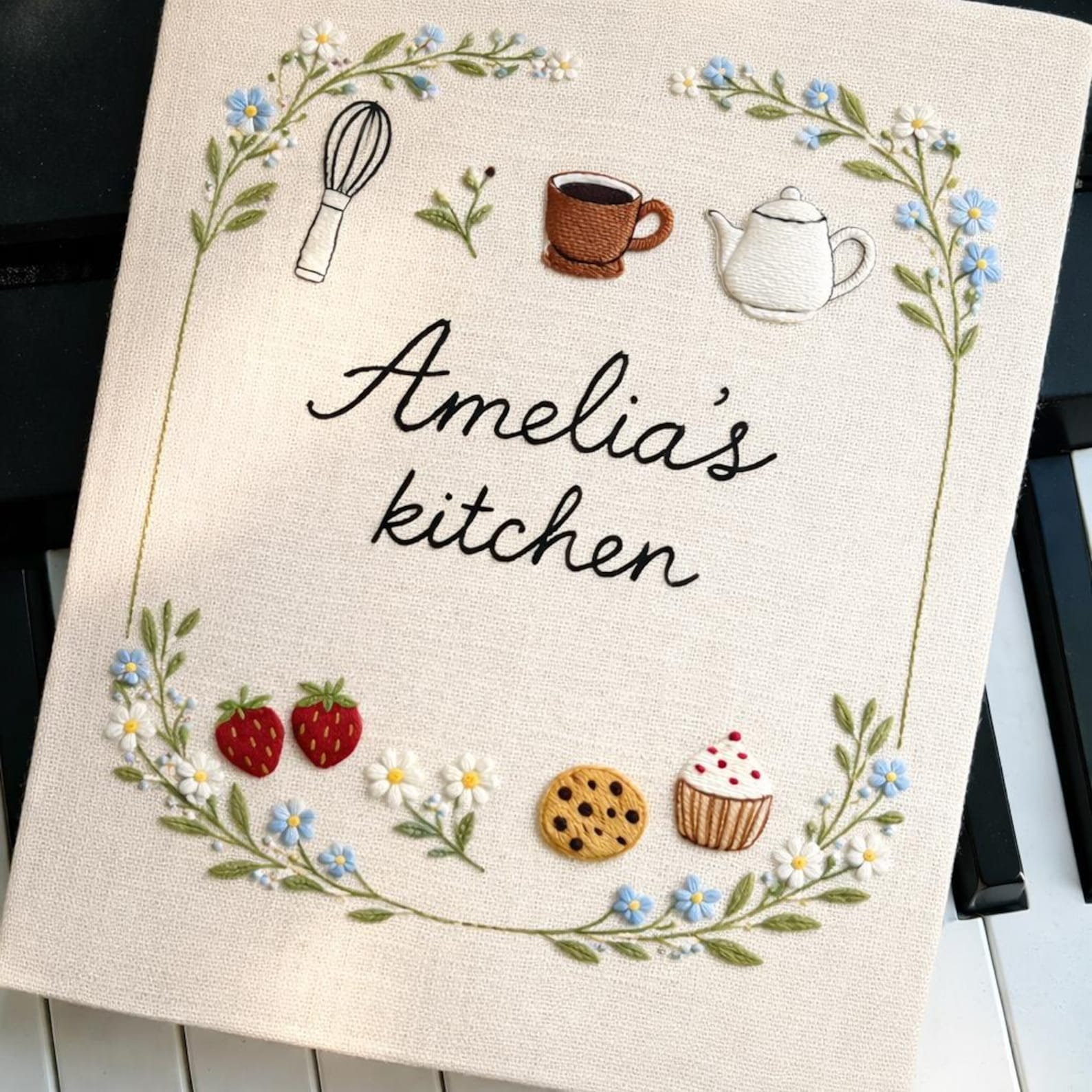 Hand embroidered recipe book featuring strawberries cookies cupcake teapot teacup whisk and floral wreath with personalized kitchen text.