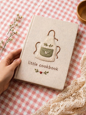 Hand embroidered recipe book featuring a minimalist cottagecore apron design on a linen hardcover notebook.