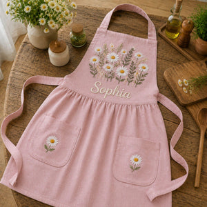 Personalized hand embroidered daisy flower apron featuring custom name embroidery, white daisies, and botanical greenery on natural linen fabric.