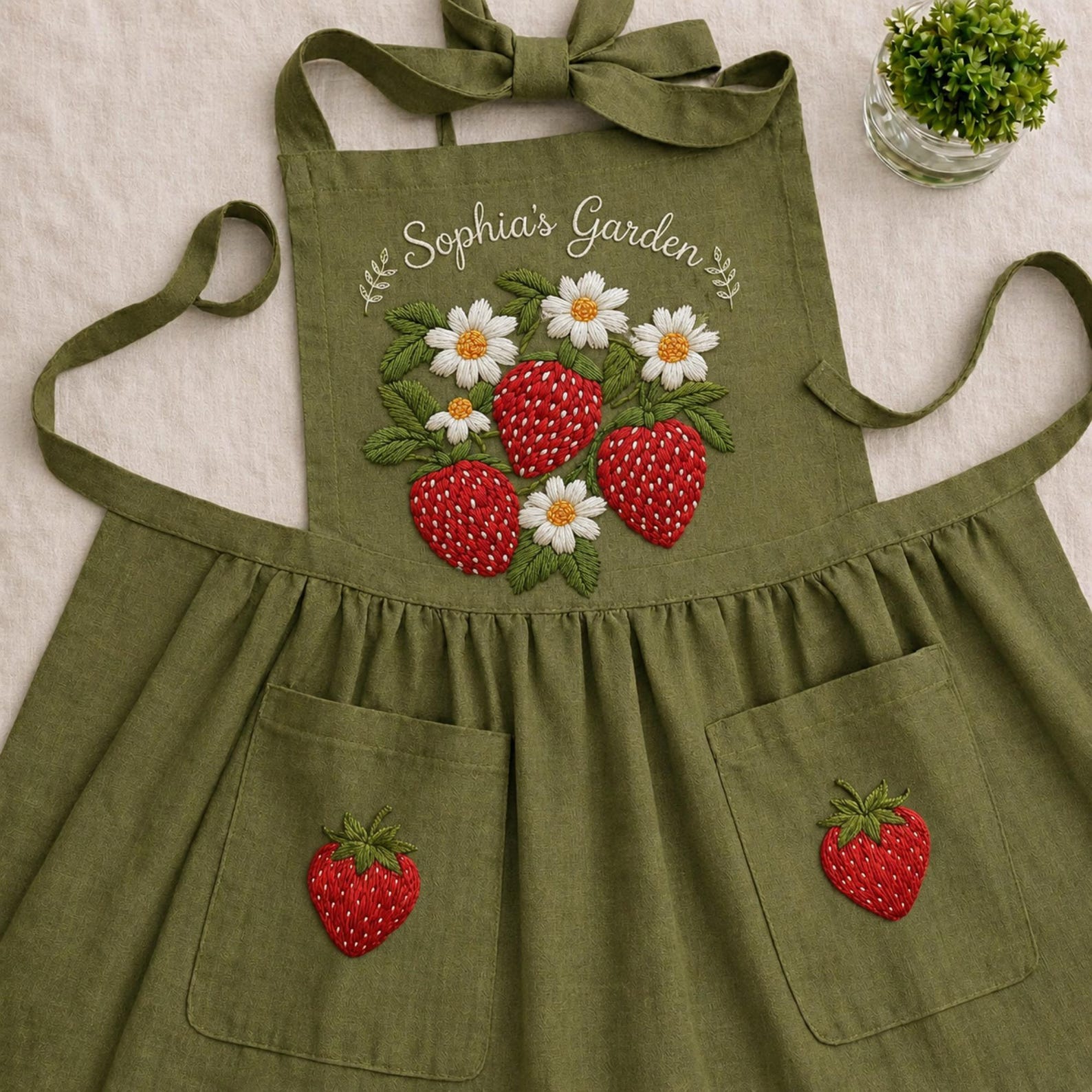 Personalized hand embroidered linen apron featuring strawberries, daisy flowers, botanical garden embroidery, and custom name personalization.