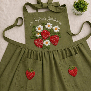 Personalized hand embroidered linen apron featuring strawberries, daisy flowers, botanical garden embroidery, and custom name personalization.