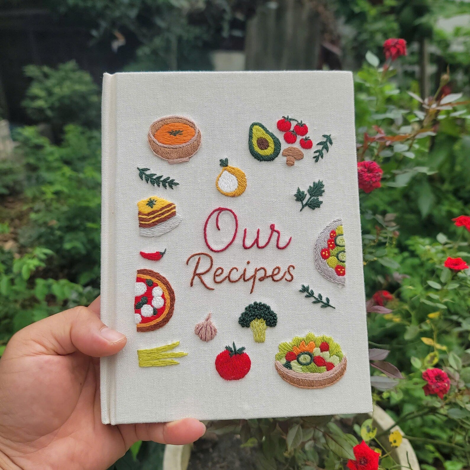 Hand embroidered recipe book featuring vegetables salads pizza lasagna soups herbs and family meal inspired food illustrations on linen cover